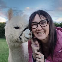 Un lama bianco accanto a una ragazza sorridente in fattoria